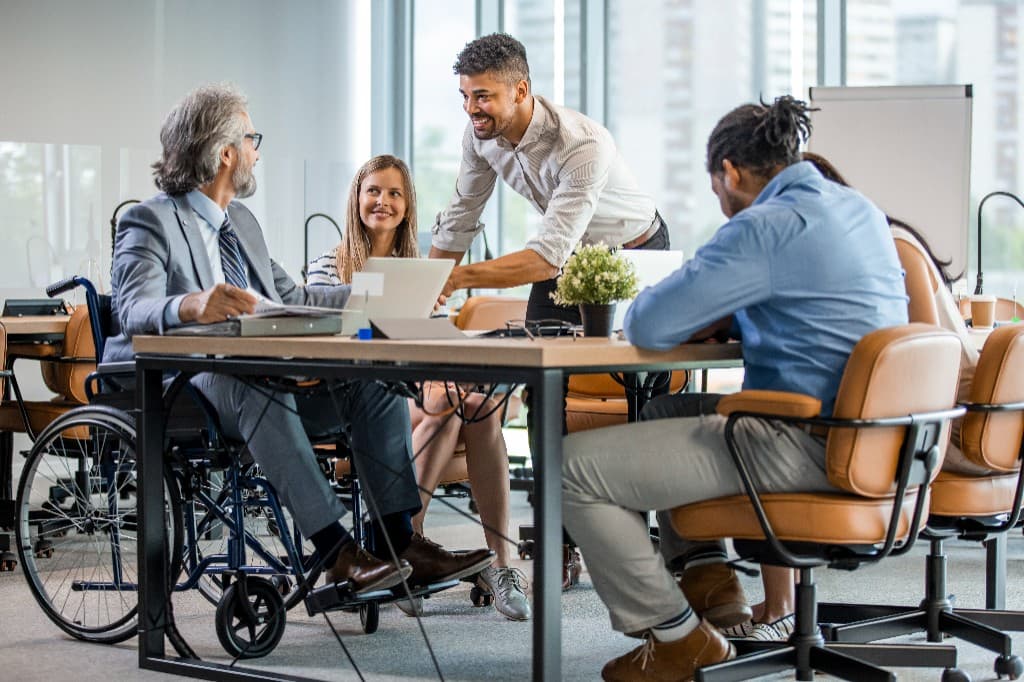 A diverse group of professional colleagues, including a man in a wheelchair, collaborating around a conference table in a bright, modern office