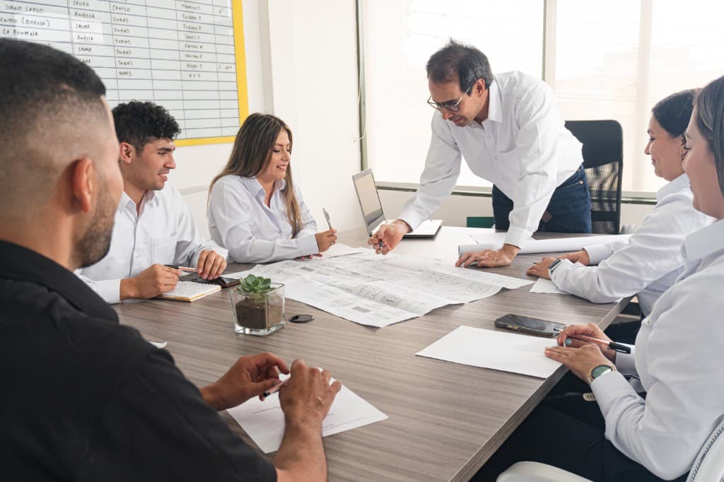 A diverse professional team collaborating around a conference table, reviewing architectural plans together in a bright office